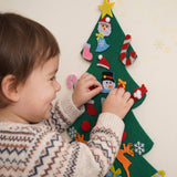 Gros plan d'un bébé qui accroche un ornement sur le sapin en feutrine